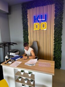 Neon "KU DO" sign against wood and green wall decor at KUDO Rent office reception area.