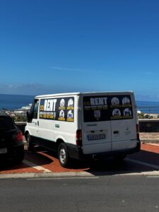 Affordable vehicle rental van on the street with ocean view, promoting KUDO Rent for car, bicycle, scooter, motorcycle, and electric scooter rentals in tourist destinations.