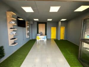 Modern indoor bike rental office with helmets display, bright yellow doors, green artificial grass accents, and colorful seating area for customers.