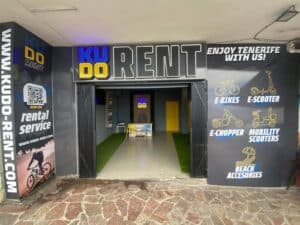 Brightly lit bicycle rental shop entrance with neon signs and colorful graphics, offering electric bikes, scooters, and beach accessories in Tenerife, with an inviting interior for customers.