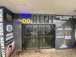 Luxurious modern storefront showcasing KUDO Rent's electric bikes, E-scooters, E-choppers, and beach accessories in Tenerife, with vibrant signage and QR code for easy rental services.