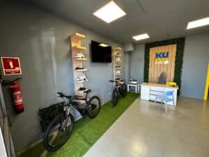 Modern office reception area with bicycles, green wall decor, and a branded KU Rent backdrop, featuring a sleek desk and relaxing seating, ideal for bike rentals and coworking services.
