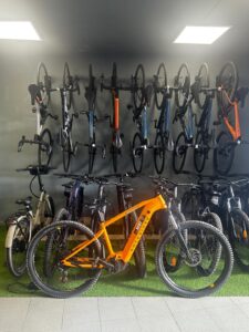 Gray wall with mounted cycling bikes, including an orange mountain bike in the foreground at KUDO Rent bike rental shop.