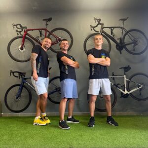 Professional bike rental team at KUDO Rent, standing in front of a wall with mounted bicycles, ready to assist customers with premium bicycle rentals for cycling enthusiasts and outdoor adventures.