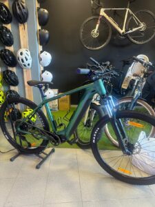 Electric mountain bike on display at KUDO Rent bike shop with bike helmets and accessories in the background.
