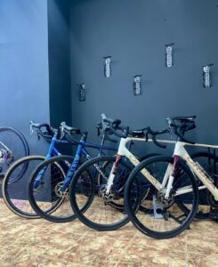 Blue and white road bicycles with flat handlebars, mounted on a bike rack in a bike storage room with wall hooks, ideal for mountain or road cycling enthusiasts, promoting bike rental services.
