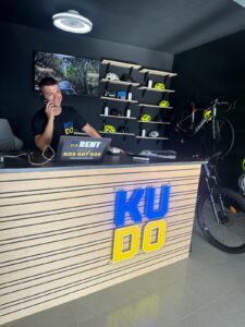 Professional bike rental shop reception with bicycle helmets, bikes, and digital signage, emphasizing cycling gear and bike rentals at KUDO Rent.