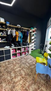 Modern bike shop with cycling gear, helmets, and accessories displayed on shelves and racks. Includes shoes, bikes, and colorful chairs, perfect for bicycle rentals and customer service.